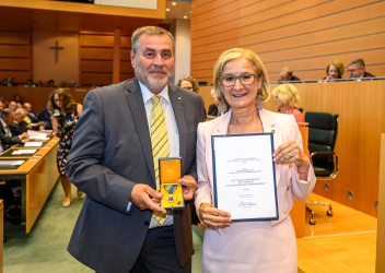 Foto von Gerhard Nachförg und Johanna Mikl Leitner, sie übergibt ihm eine Urkunde und das goldene Ehrenkreuz