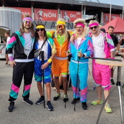 Gruppenfoto des 3er Männerteams. Alle drei sind haben lange Perücken und bunte Trainingsanzüge an.