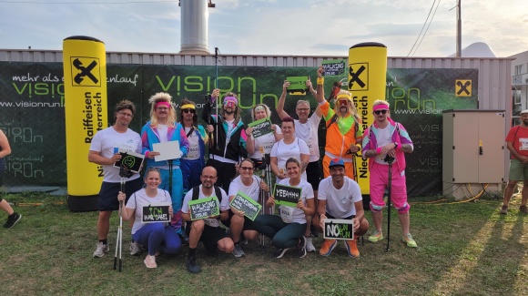 Gruppenfoto unserer Mitarbeiter*innen, die beim Vision Run mitgemacht haben. Jeder hält ein Schild mit einem lustigen Spruch drauf in der Hand.