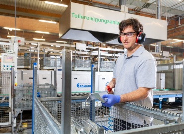 Ein Mitarbeiter der Metallabteilung mit Gehörschutz und Sicherheitsbrille steht in der Produktion und arbeitet