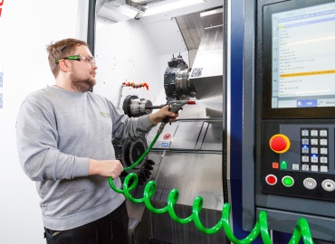 Ein Mitarbeiter der Metallabteilung mit Schutzbrille wäscht eine Maschine mit einem Schlauch aus